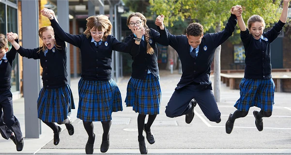 Group of schoolchildren in uniforms happily jumping together outdoors.