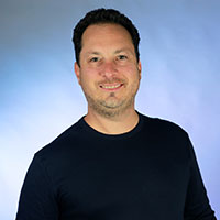 Smiling man in a dark shirt standing against a light blue background