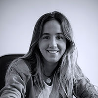 Smiling woman with long hair sitting indoors, wearing a casual jacket