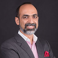 Smiling man with a beard in a suit jacket and pink shirt, posing against a dark background