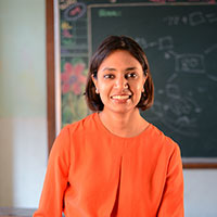 Smiling woman with short dark hair wearing an orange top in a classroom setting