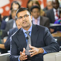 Man in a suit speaking at an event with audience in the background