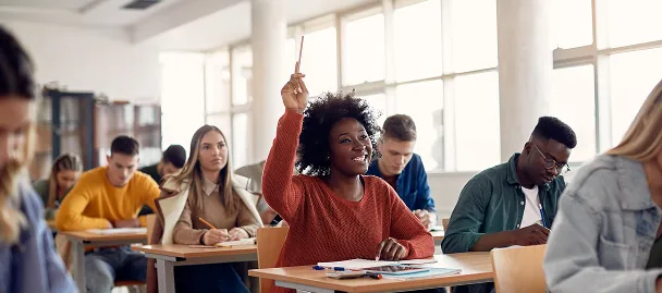 Student raising her hand in a classroom while classmates work at their desks